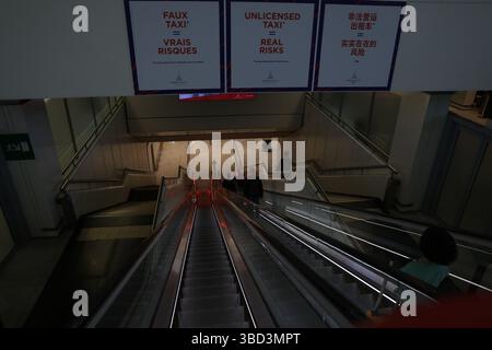 Una scala mobile elegante e moderna scende in un livello inferiore di uno spazio pubblico, fiancheggiata da pannelli di vetro e illuminata da luci rosse. Una grossa scre Foto Stock