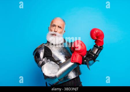 Uomo anziano con armatura medievale e guanti da boxe in posa su sfondo blu Foto Stock