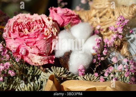 Composizione floreale con rose rosa essiccate, gusci di cotone e delicati rametti. Questo vivace display mette in risalto la bellezza naturale in un regalo creativo Foto Stock