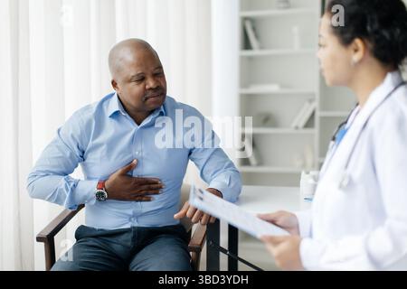 Paziente di sesso maschile nero che tiene lo stomaco, soffre di dolore addominale durante l'incontro con il medico Foto Stock