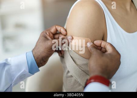 Medico che applica Plaster sul braccio di una paziente di sesso femminile nera dopo vaccino Foto Stock