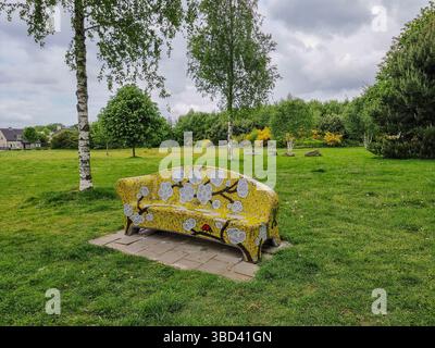 Panchina in pietra giallo brillante decorata con un mosaico (motivo floreale) su un campo di erba verde in un parco nei Paesi Bassi Foto Stock