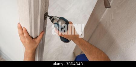 Lavoratore maschio con trapano elettrico che installa la piastra di battuta della porta in camera Foto Stock