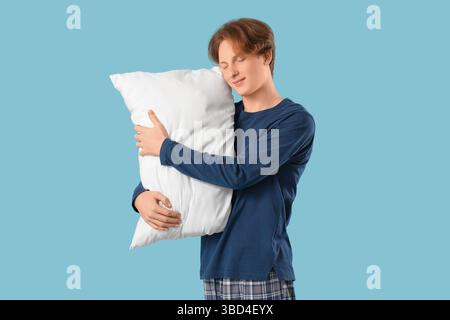Bel giovane uomo felice in pigiama con cuscino che dorme su sfondo blu Foto Stock