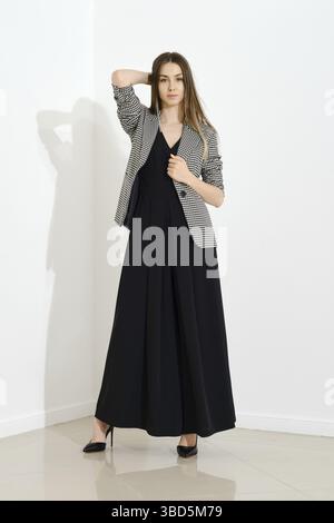 Ritratto interno di una giovane donna alla moda con abito lungo nero e giacca a scacchi Foto Stock