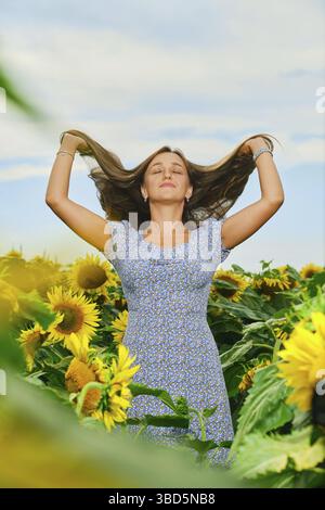 Bella giovane donna caucasica che solleva lunghi capelli scuri in campo di girasole Foto Stock