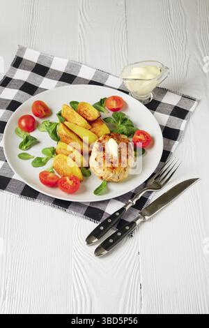 Cotoletta di pollo fritta con fette di patate servite con pomodoro ciliegia e insalata di mais. Cibo tradizionale bielorusso, carne macinata arrosto e patate Foto Stock