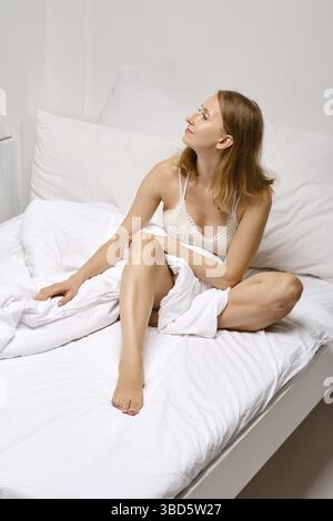 La donna addormentata si siede a letto e guarda in su Foto Stock