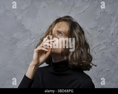 Donna giovane e pusiva con capelli ricci che guardano e toccano il mento Foto Stock