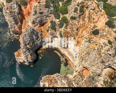 Foto aerea di una piccola spiaggia di sabbia con ombrelloni circondata da scogliere a Ponta da Piedade Foto Stock