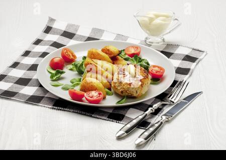 Cotoletta di pollo fritta con fette di patate servite con pomodoro ciliegia e insalata di mais. Cibo tradizionale bielorusso, carne macinata arrosto e patate Foto Stock