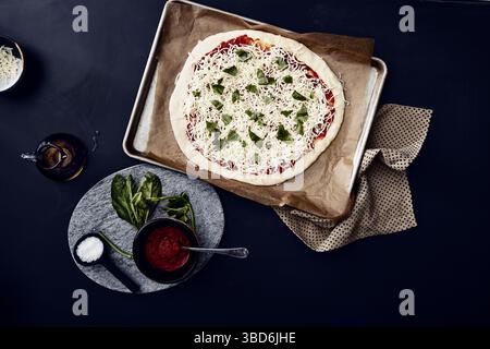 La persona allunga l'impasto su una superficie scura spolverata di farina. Foto Stock