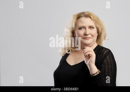 Donna matura in cardigan lavorato a maglia su sfondo grigio studio Foto Stock