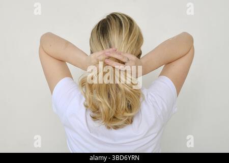 Vista posteriore di una donna che fissa i capelli e si lega un nastro sui suoi capelli Foto Stock