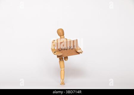 Uomo di legno a una gamba che regge un cartoncino di carta con cambio di testo su sfondo bianco, cambiamenti di vita Foto Stock