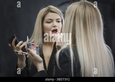 Donna che applica il rossetto liquido guardando allo specchio Foto Stock