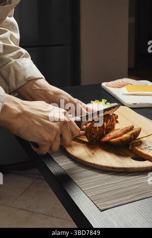 Vista laterale ravvicinata delle mani di una donna irriconoscibile che taglia il pomodoro per un sandwich Foto Stock