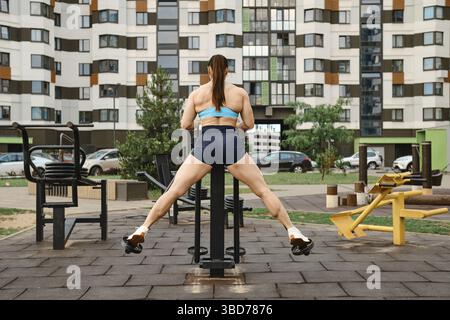 Vista posteriore della donna che fa esercizio sui muscoli delle gambe nei campi sportivi in un complesso residenziale Foto Stock