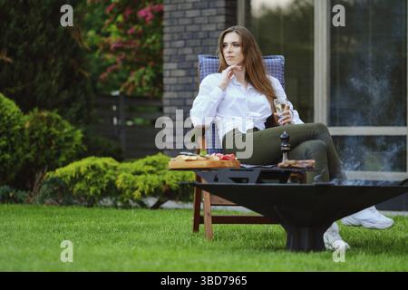 Bella giovane donna si siede su sedia pieghevole sul cortile e guardando al lato Foto Stock