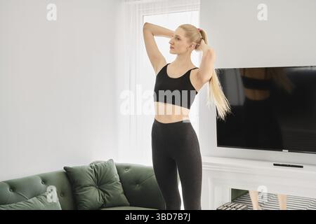 La donna bionda attiva fa esercizi di torsione in appartamento luminoso Foto Stock