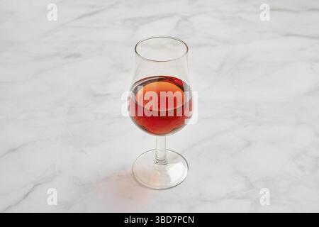 Un vetro cristallino riempito con un ricco brandy su una superficie liscia in marmo. La luce naturale si riflette sul vetro, esaltandone il colore e creando un Foto Stock