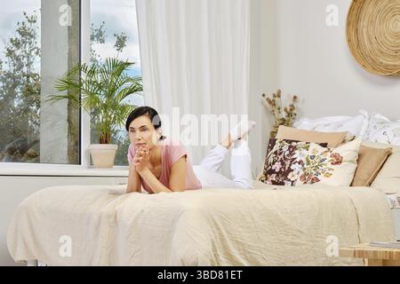 Ritratto di donna pensiva in abiti casual sul letto a casa Foto Stock