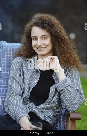 Ritratto all'aperto di giovane donna sorridente con capelli ricci lunghi Foto Stock