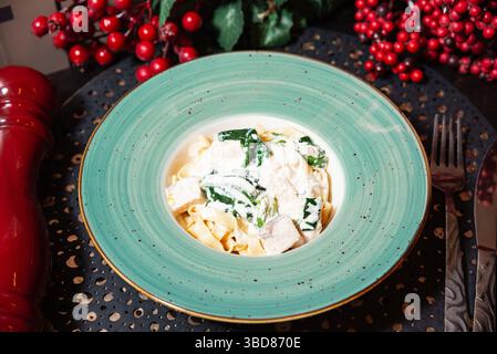 Tagliatelle servite con salsa bianca cremosa, teneri pezzi di pollo e spinaci freschi, placcati in un recipiente turchese. Foto Stock