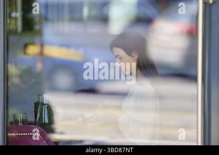 Vista attraverso la finestra del caffè a giovane donna seduta interno Foto Stock