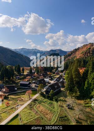 Drone view of Ainokura village in Toyama, Japan on a crisp autumn morning with gassho houses, colorful trees, mountain backdrop and bright sky above Foto Stock