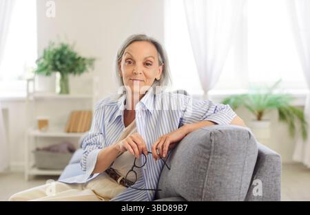 Ritratti di anziani sorridenti e concentrati, donne anziane che tengono gli occhiali a casa Foto Stock