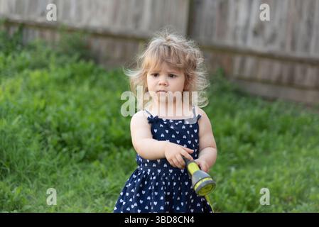 La bambina tiene il tubo dell'acqua per spruzzare l'erba nel giardino del cortile Foto Stock