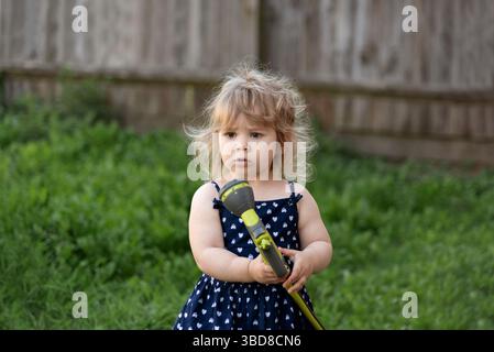 La bambina tiene il tubo dell'acqua per spruzzare l'erba nel giardino del cortile Foto Stock