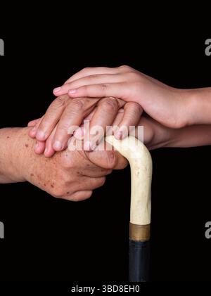 Toccante momento di una mano giovane che tiene le mani anziane su un bastone Foto Stock
