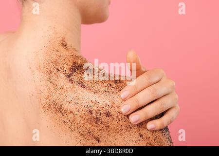 Donna che applica il body scrub sulla spalla su sfondo rosa, primo piano Foto Stock