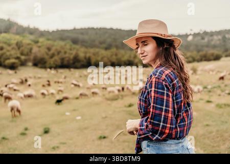 Una donna che indossa un cappello di paglia si trova in un campo di pecore Foto Stock