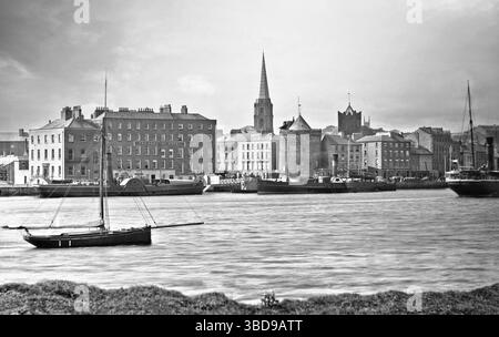Una fotografia dei primi anni del XX secolo delle banchine che attraversano il fiume Suir mentre scorre attraverso Waterford City, in Irlanda. Al centro si può vedere la Torre di Reginaldo, costruita nel XIII o XIV secolo dagli anglo-normanni dopo la conquista di Waterford, in Irlanda, in sostituzione di una precedente fortificazione vichinga. Foto Stock