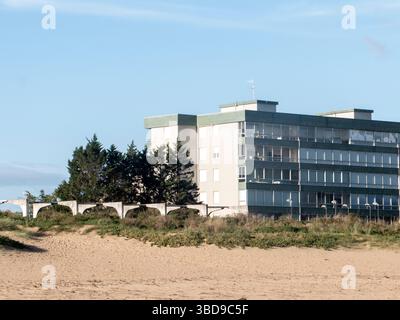 Moderno hotel fronte spiaggia che sorge sopra una costa sabbiosa punteggiata di pini, offrendo una tranquilla fuga sul mare Foto Stock