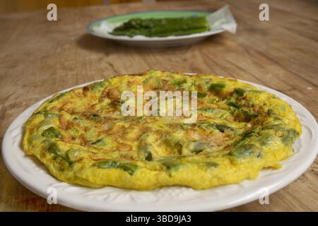 Una deliziosa omelette fatta in casa con asparagi verdi freschi e saporito parmigiano, servita su un piatto bianco su un rustico tavolo di legno. Nel backgrou Foto Stock