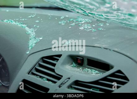Vetri rotti sparsi sul cruscotto dell'auto polveroso sotto il parabrezza incrinato. Abitacolo del veicolo dopo una collisione frontale. Foto Stock