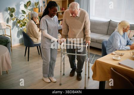 Assistere l'uomo anziano con Walker in una casa di cura confortevole Foto Stock