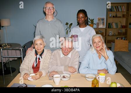Ritratto degli anziani che sorridono al tavolo con l'operatore sanitario Foto Stock