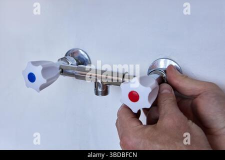 La persona sta montando due rubinetti inutilizzati sui vecchi raccordi per tubi, le mani fissano il corpo in metallo lucido con manici in plastica ai collegamenti idraulici a parete. Foto Stock