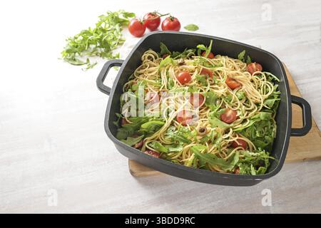 Spaghetti con pomodori, rucola e olive in un'ampia ciotola nera su un tavolo dipinto di bianco, pasto vegetariano mediterraneo fatto in casa, spazio copia, selezione Foto Stock