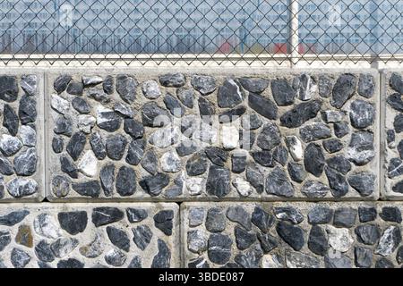 Dettaglio orizzontale di una parete di roccia sfondo costituito di piccole e frastagliate rocce granitiche con piastrelle e boiacca giunti e una recinzione sulla parte superiore Foto Stock