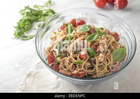 Insalata mediterranea di spaghetti con pomodori, rucola, mozzarella, olive e basilico in una ciotola di vetro su un tavolo dipinto di bianco, spazio per copiare, sel Foto Stock