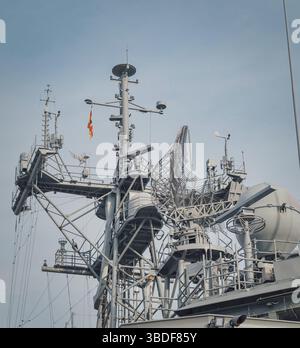 Vista ravvicinata dell'albero di una nave navale con radar e apparecchiature di comunicazione avanzate, comprese antenne e sensori. Una bandiera indica la nazionalità o. Foto Stock