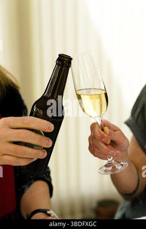 Vista in dettaglio di due donne che fanno un brindisi con una bottiglia di birra e un bicchiere di champagne Foto Stock