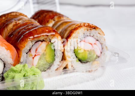 Sushi assortiti ricoperti di gamberi e glassa di anguilla, ripieni di avocado e riso, serviti in una scatola di plastica trasparente con wasabi. Sushi roll californiano Foto Stock