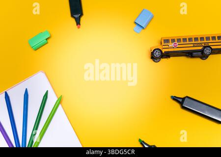 Materiale scolastico, tra cui pastelli, matite colorate, pennarelli, quaderno e uno scuolabus giallo, disposti su uno sfondo giallo brillante con fotocopiatrice Foto Stock